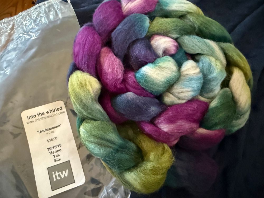 A braid of spinning fiber from @intothewhirled yarn in the color “Unobtainium” which is green, purple, and blue. The blend is 70/15/15 Merino/Yak/Silk