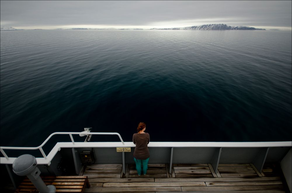 Female scientist looking out to the open ocean from the deck of a ship.