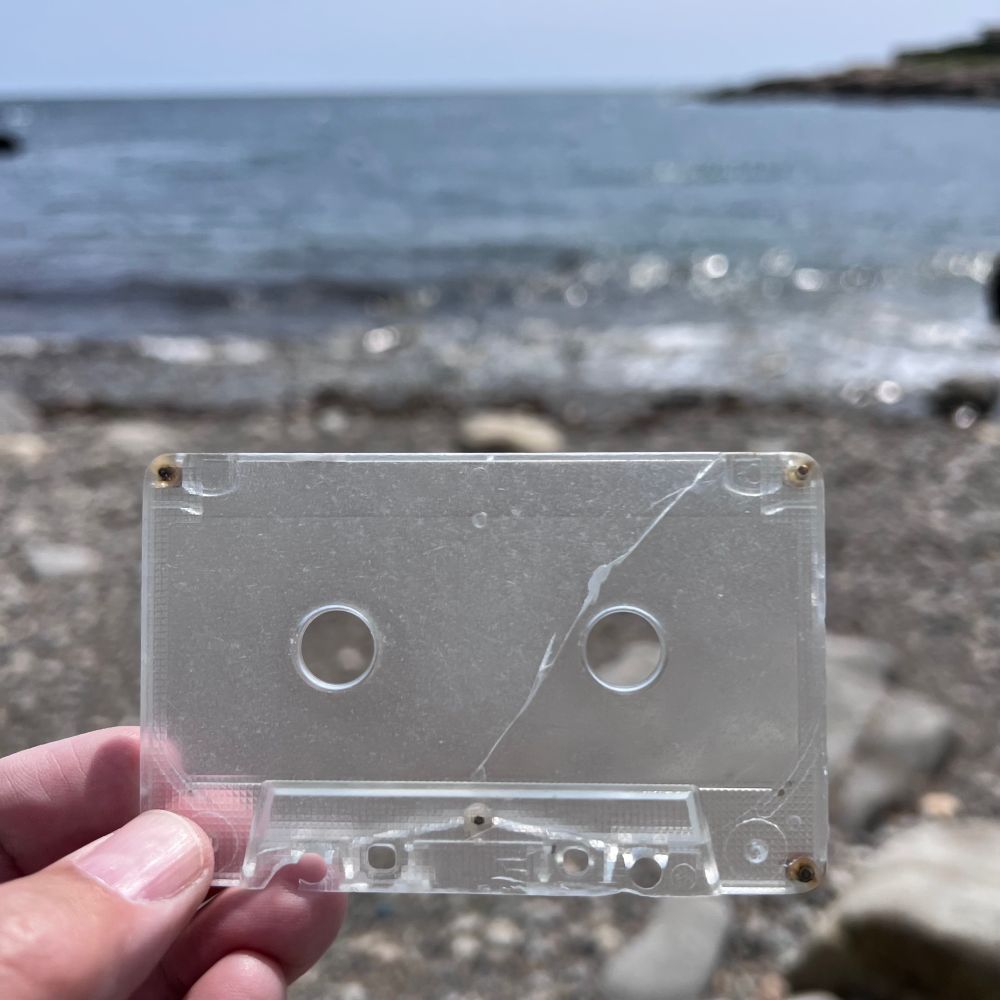 Weathered plastic part of a cassette tape held up to the sky on a beach