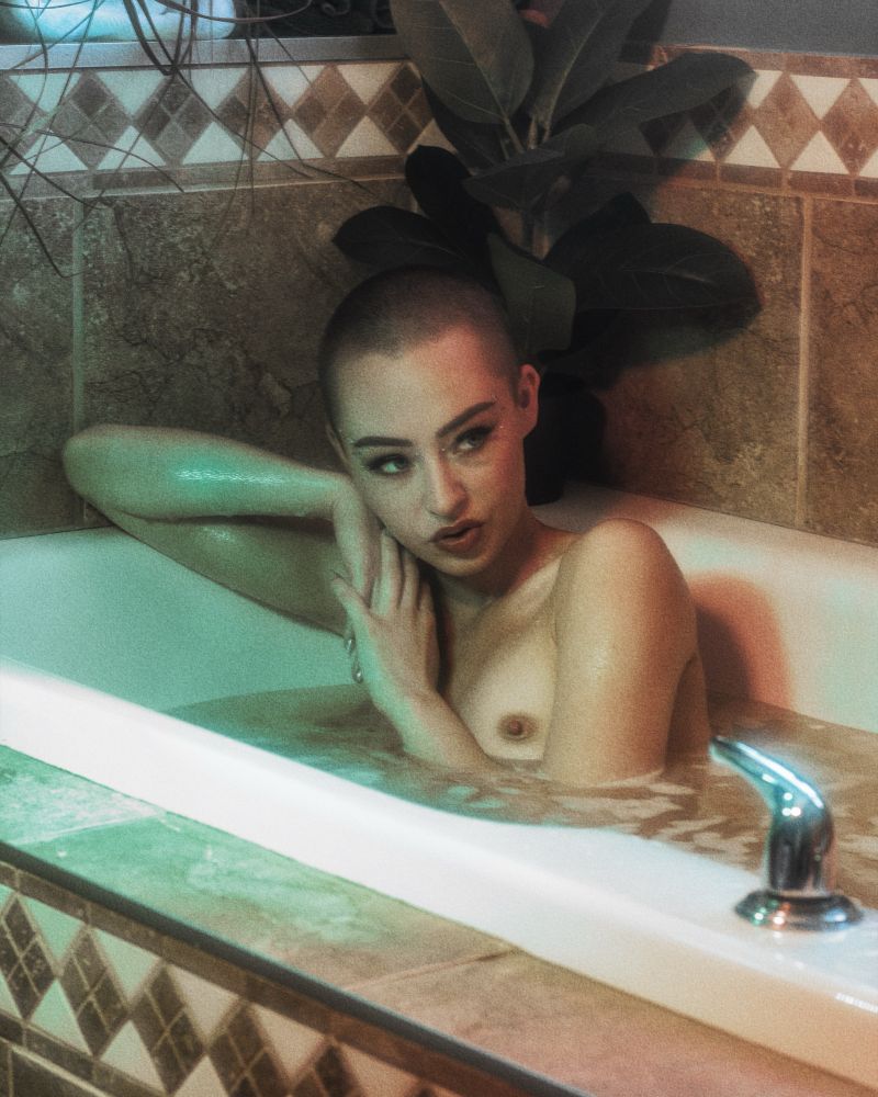 Darla DeVeaux sits naked in a bath (as one typically does). Her right arm sits on the edge of the tub and her face rests gently on her arm. One of her breasts is exposed, showing a glimpse of nipple. Gasp!