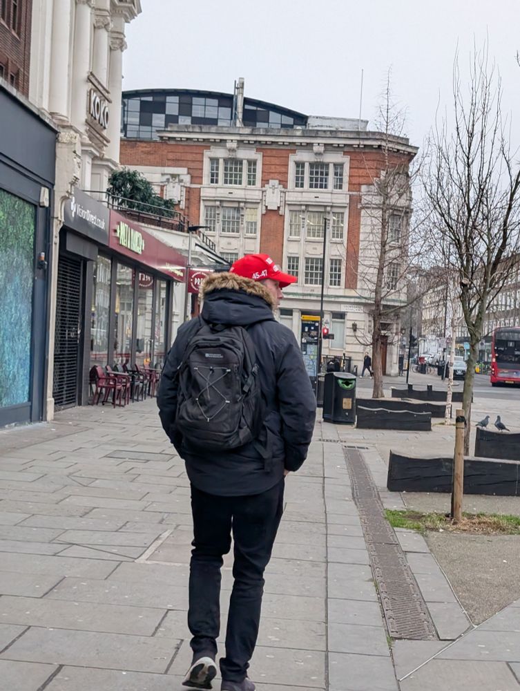 A man walking down a pavement wearing a MAGA hat