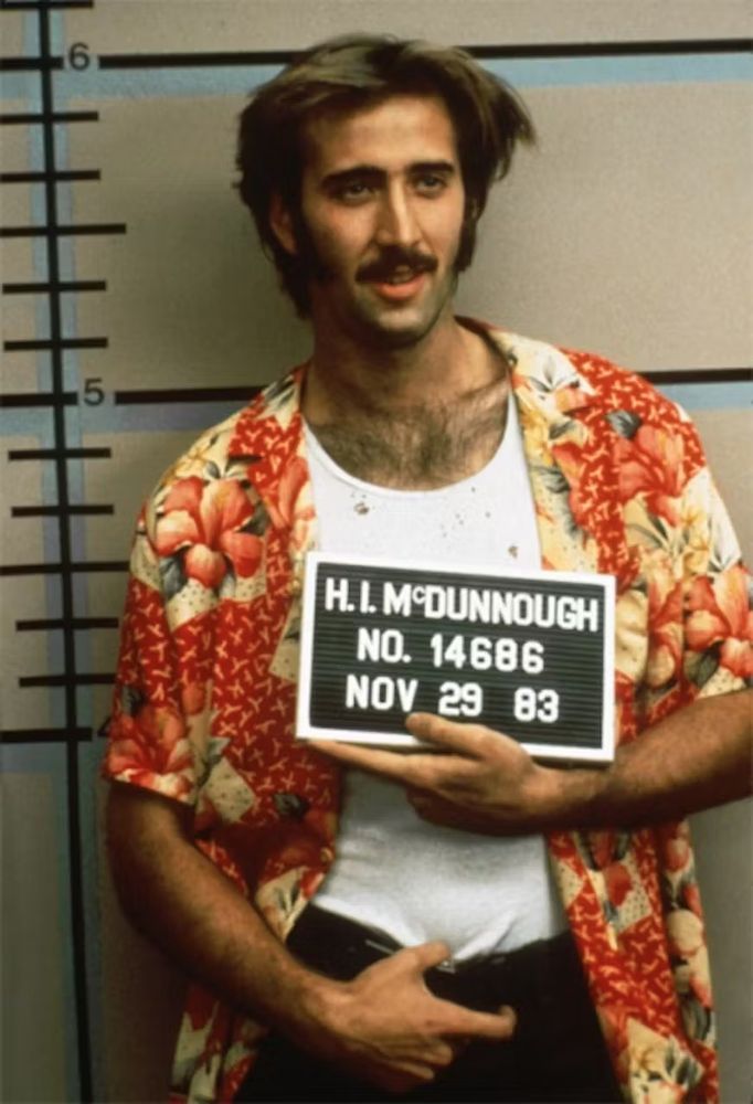 Nicholas Cage as H.I. McDunnough. He is getting his mugshot taken.