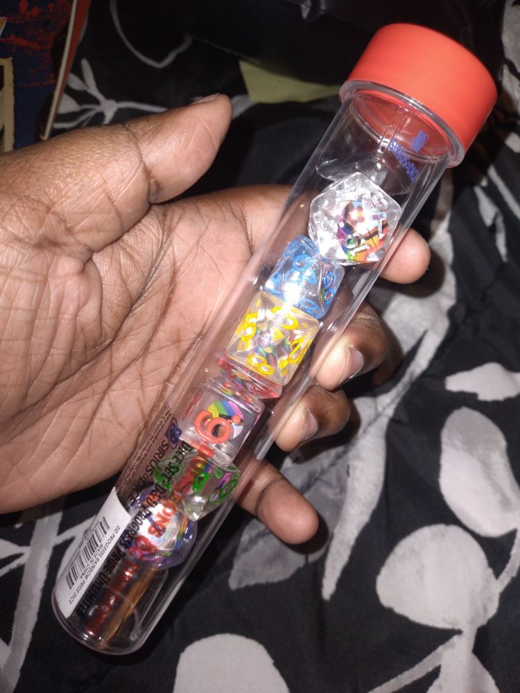 A container of various multi-sided dice, all of which are clear and have the LBGTQIA+ flag within them. 