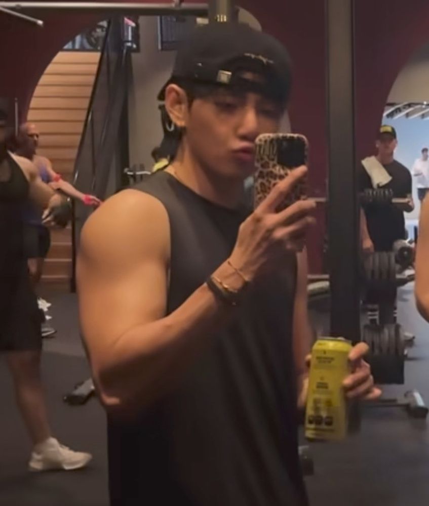 taehyung taking a video at the gym, his bicep looking huge as hell as he makes a kissy face, wearing a black tank and a backwards cap