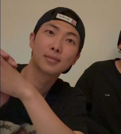 namjoon wearing a ball cap backwards looking cute and hot as hell all at the same thine, leaning to the side slightly, black shirt one, soft smile on his face 