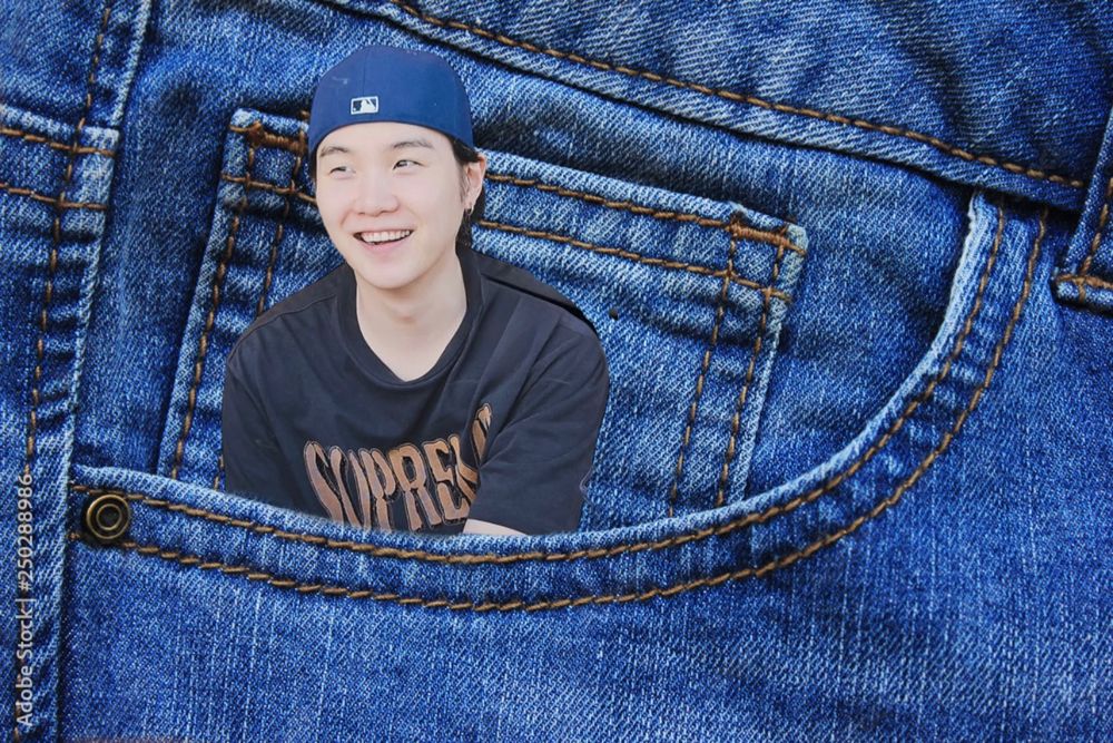 yoongi photoshopped inside the top of a jean pocket. he’s smiling wearing a backwards ball cap and navy blue supreme shirt. 