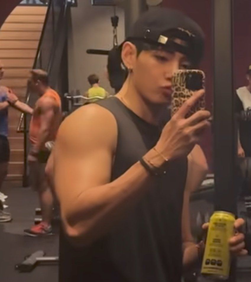 taehyung taking a video at the gym, his bicep looking huge as hell as he makes a kissy face, wearing a black tank and a backwards cap