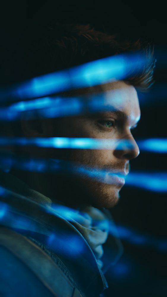 A virtual photo of Cal Kestis from Jedi: Survivor. He is in profile, his face emerging from darkness. Rays of blue light stream across the photo, framing his eyes and reflecting off his face.