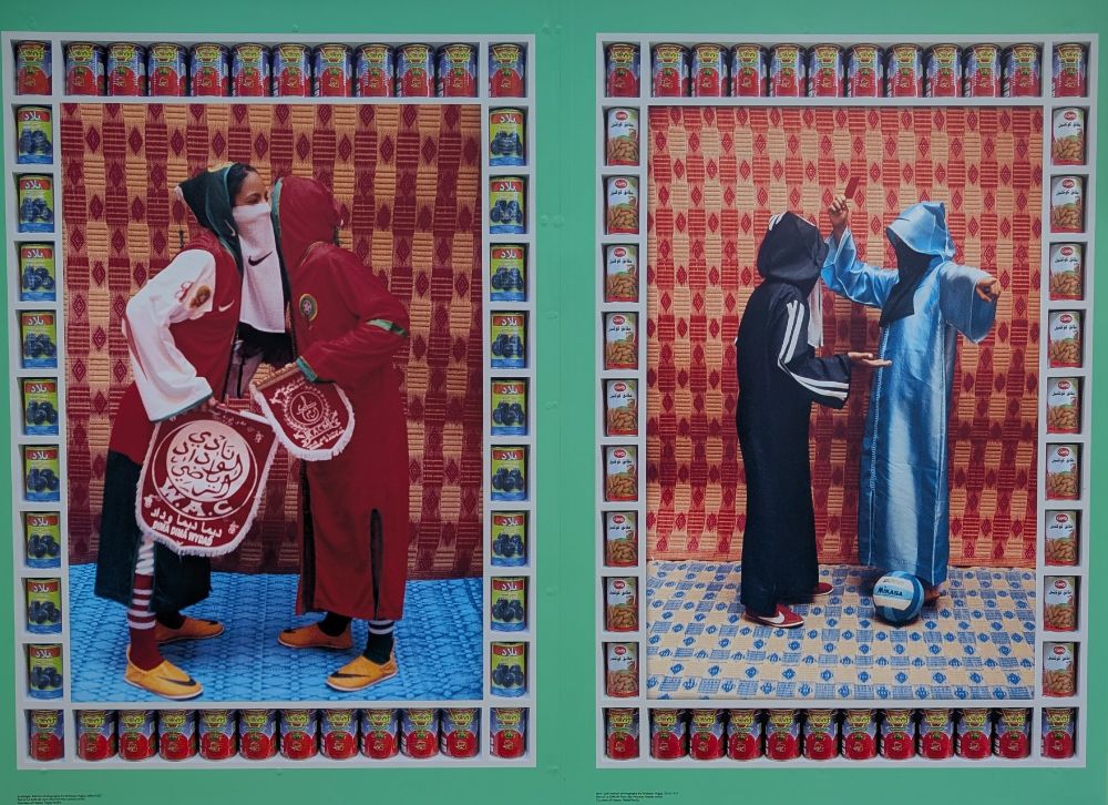 Two photographs framed by cans of vegetables. The left (Exchange) shows two women, veiled and in long sportswear, exchanging a word while holding team pennants. 

Right picture (Red Card) again shows two women, veiled, but one on the right in light blue holds a referee's red card and has a football near her feet, while the one in the left (in black) makes an appeal