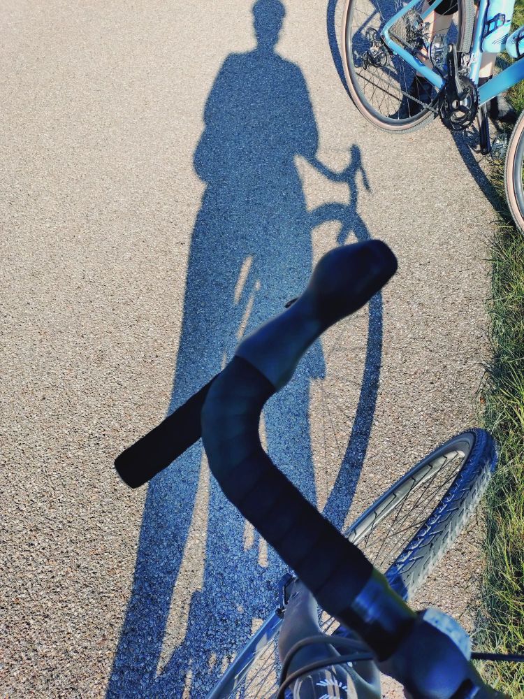 Bild von einem Gravelfahrer. Man sieht den Lenker und den Schatten des Fahrers auf der Straße 