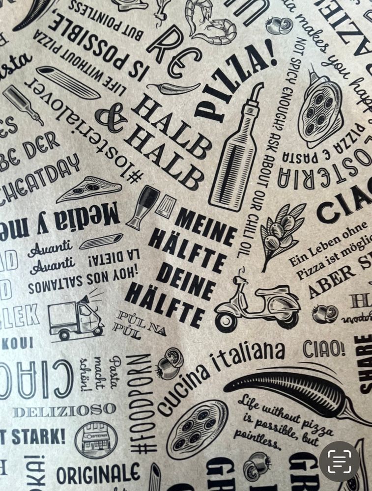 Eine Unterlage aus Papier die in einer Pizzeria auf den Tischen liegt. Das Papier ist über und über mit lustigen kleinen Sprüchen und Zeichnungen bedruckt wie zum Beispiel „Meine Hälfte, deine Hälfte“, Zeichnungen von Motorrollern, Chilis, kleinen Lieferautos.