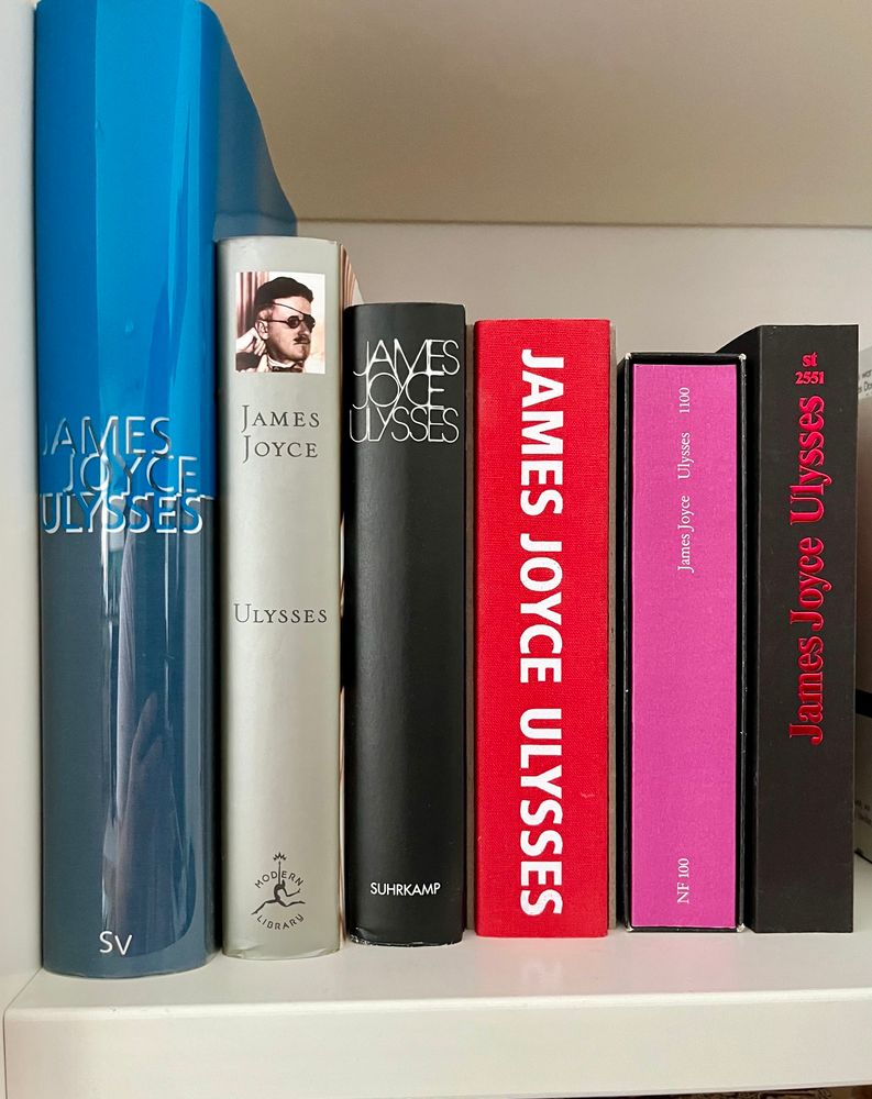 In einem Regal stehen sechs verschiedene Ausgaben des Romans „Ulysses“ des irischen Schriftstellers James Joyce. 