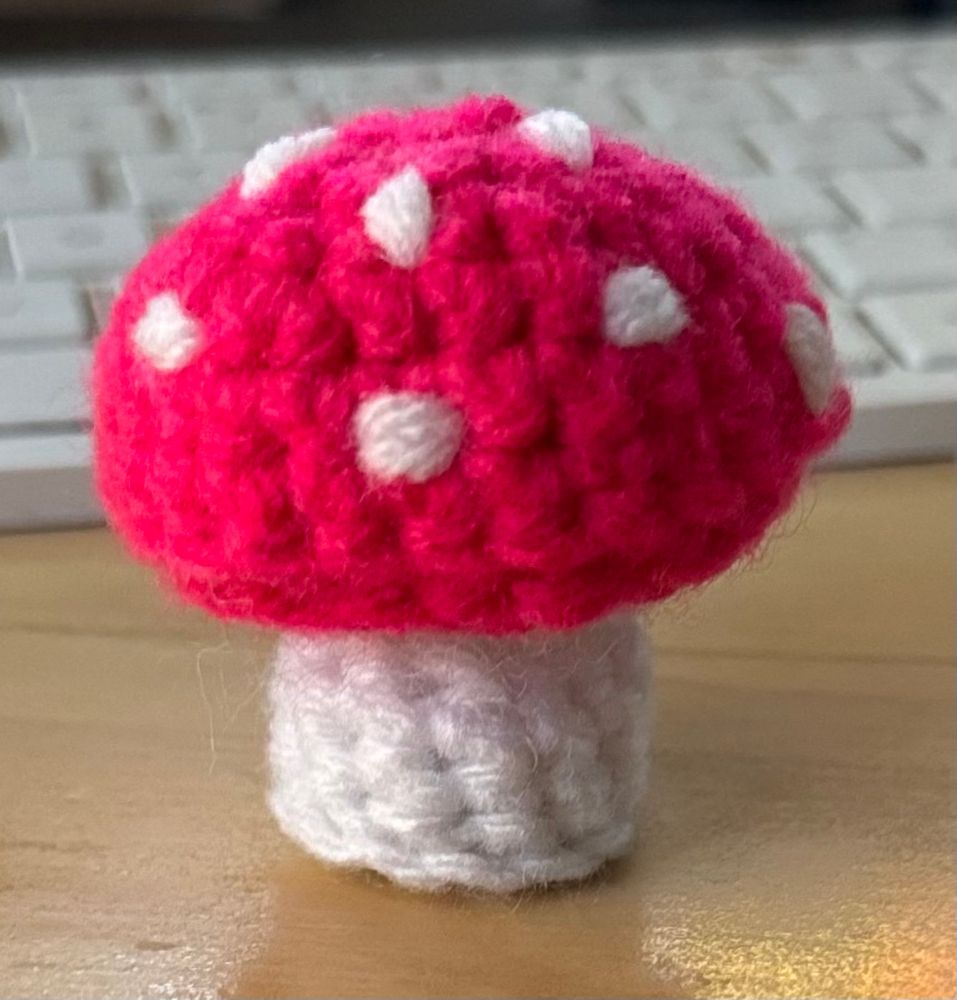 Crocheted mini mushroom; hot pink cap with white spots and a white stem.