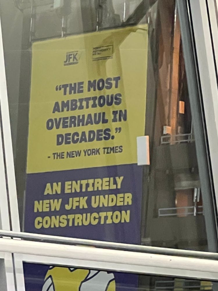 a yellow and blue sign reading: “ “The most ambitious overhaul in decades.”- New York Times        An Entirely New JFK Under Construction 