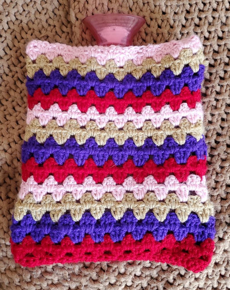 A crocheted sweater for a hot water bottle made of three color stripes. 