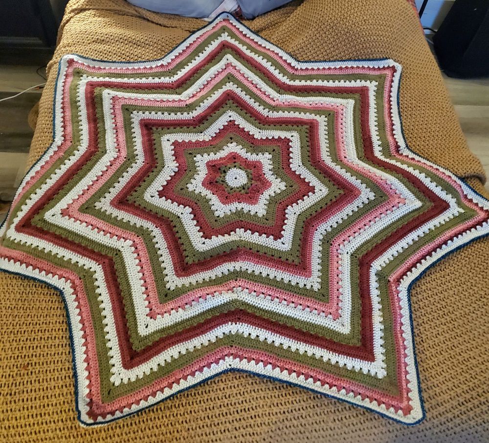 A crocheted star blanket with three colors alternating in the pattern as stripes. 