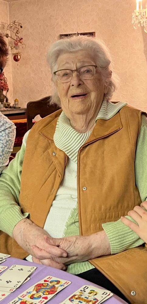 Der 98. Geburtstag im letzten Jahr. Ältere Dame sitzend an einem Tisch, sie lächelt in die Kamera. Vor ihr liegen Spielkarten. 