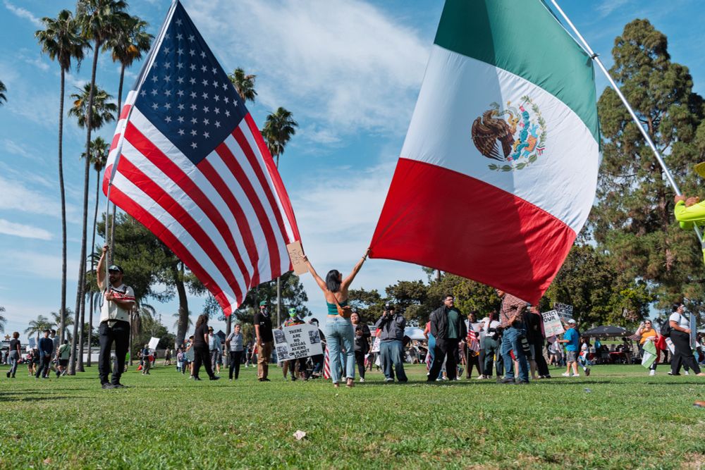 A woman poses for a photo between two large American and Mexican flags at the No Kings protest in Anaheim, Ca on 6/14/25.