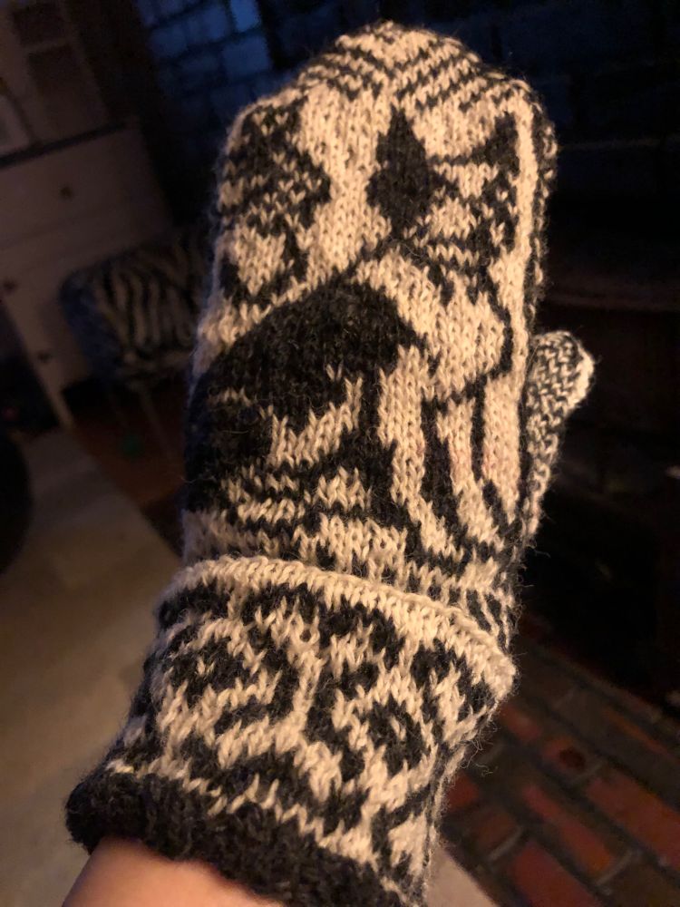 A black and white mitten with a Boston terrier knitted into it