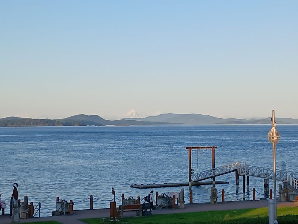 View of the blue ocean with snow-clad mountain in the distance. A silouette of a pier in the foreground.