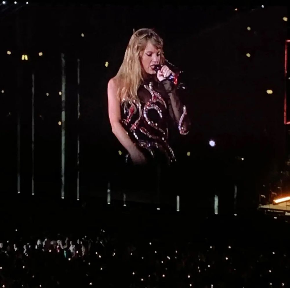 Taylor Swift in a black and gold dress singing into a microphone
