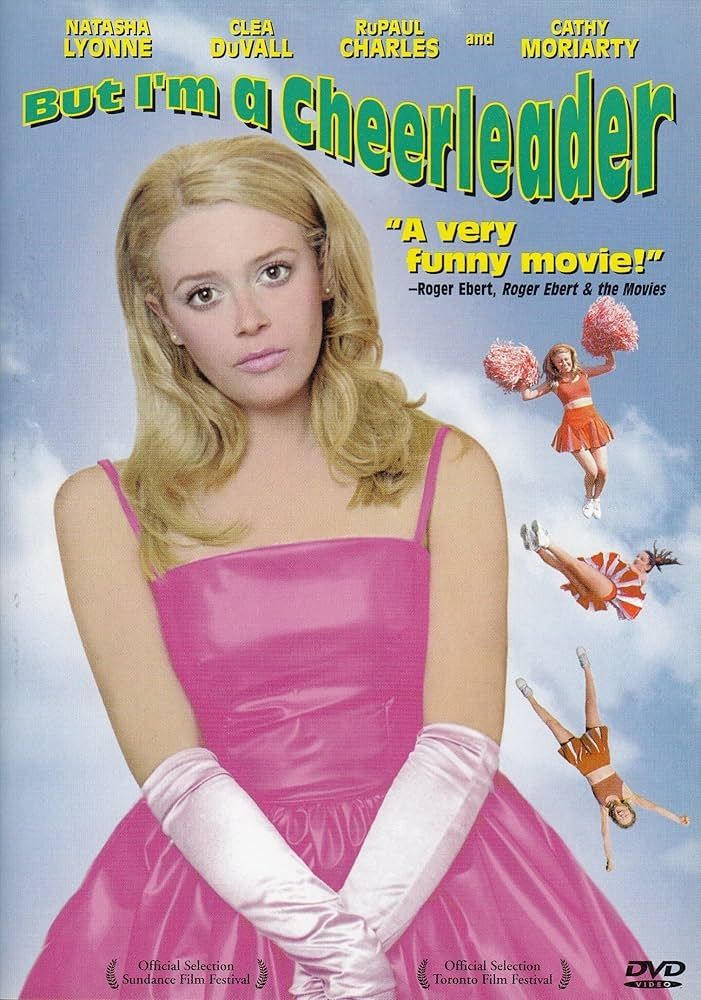 The DVD cover of "But I'm a Cheerleader" most of the image is taken up by the main character, a blonde teenager, in a pink dress with white gloves. Behing her versions of herself tumble in the air in an orange and white cheer uniform. 