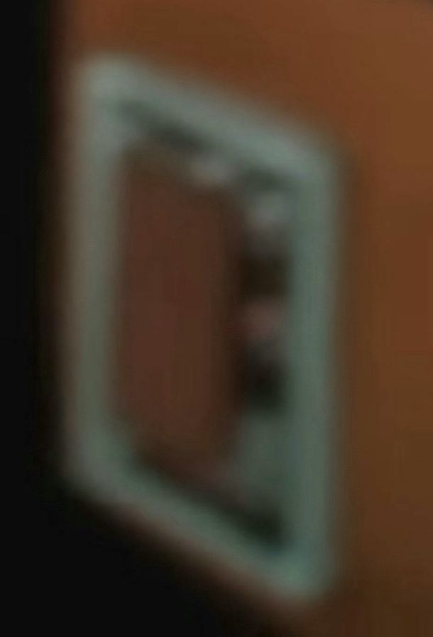Very blurry closeup of the item on the table in the OP's post. It is impossible to tell exactly what it is but it is rectangular and could be a single item or multiple items laying on top of each other. 