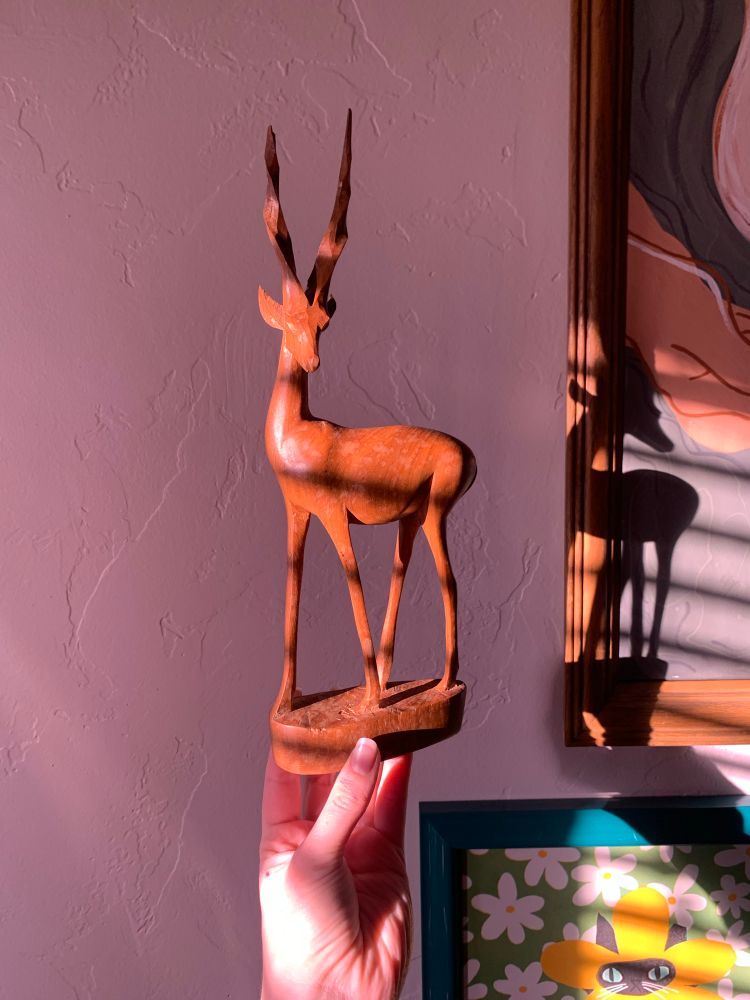 Nat holding a whittled wooden antelope (honestly, unsure of the exact type of animal… but it is definitely a horned bovid of sorts).