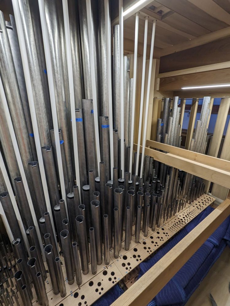 Interior of pipe organ swell box chamber showing metal pipes and wind lines feeding wood pipes mounted above the roof