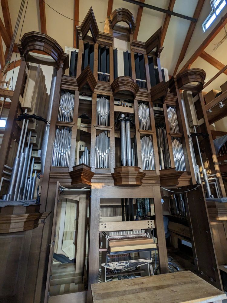 Exterior of pipe organ under construction, showing wood case, some polished facade pipes, and through gaps with out facade pipes, various interior pipes, wind lines, and other components can be seen 