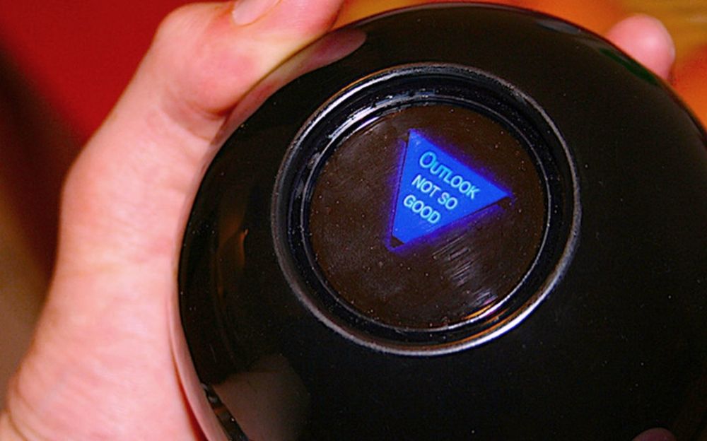 A hand holding a Magic 8 Ball that says "Outlook not so good."