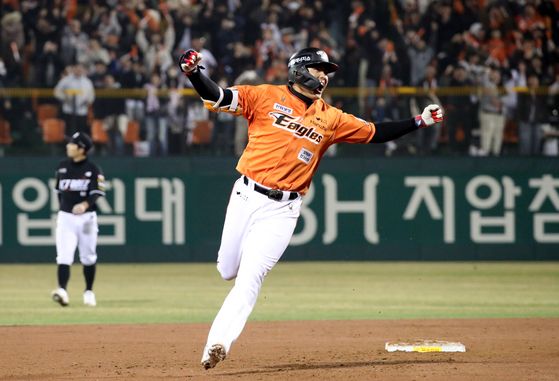 Hanwha Eagles player rounding the bases while celebrating a homerun. He's wearing an orange jersey with white pants and a black helmet.