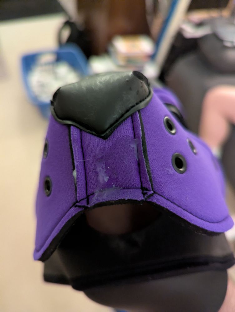 Closeup of a purple and black Mr. S Leather pup hood with cum smear all over the muzzle and a blurry background.