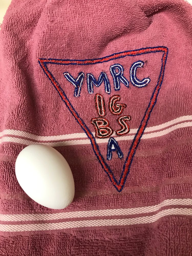 Pink towel embroidered with s large towel embroidered with “YMRCIGBSA” which stands for “Young Men’s Reformed Cultists of the Ichor God Bel Shamharoth Association.”
And a Hard Boiled Egg