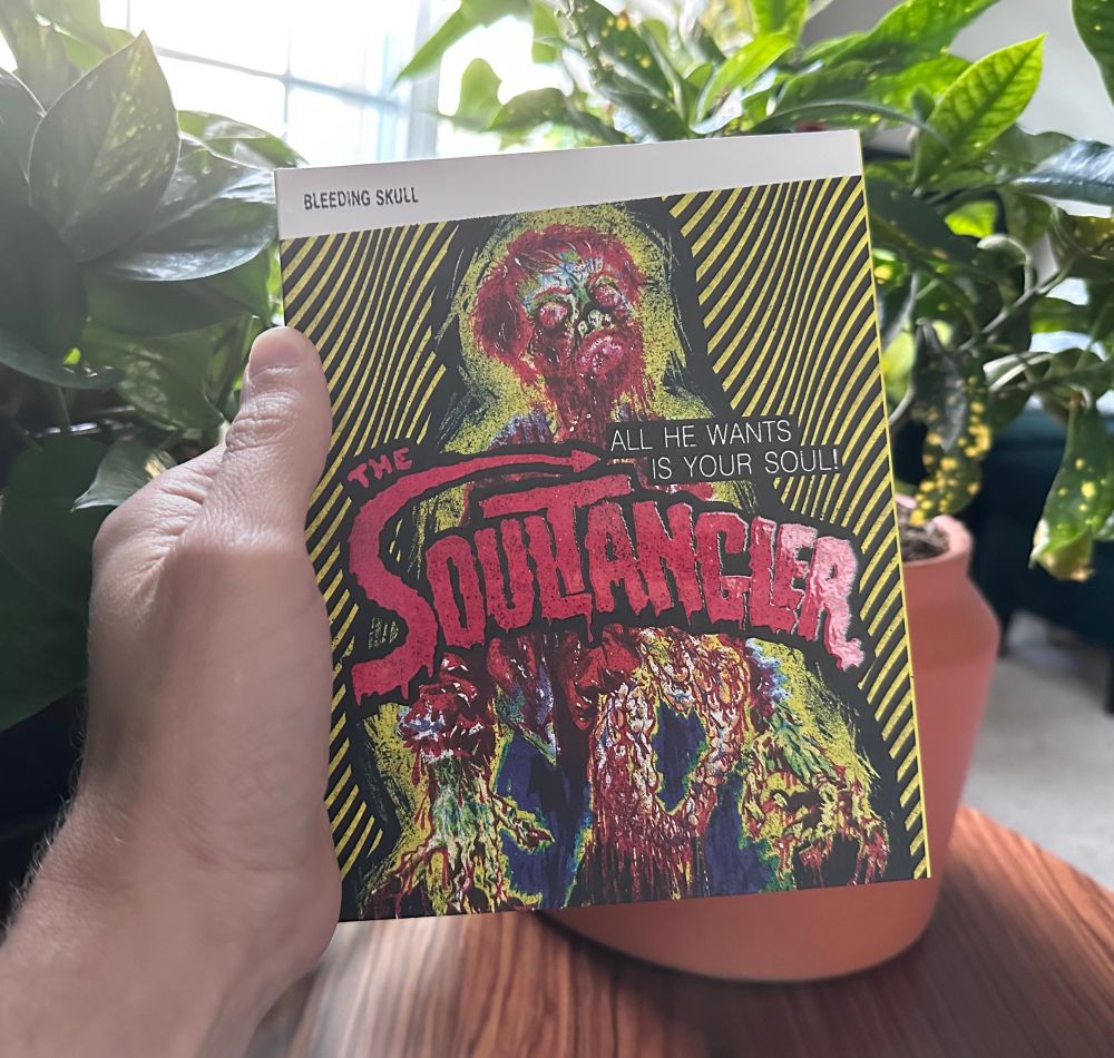 A hand holding a slipcovered blu-ray. On its cover in day-glo coloring is a horribly melty looking man. The title The SOULTANGLER is embossed on its cover with the tagline: All He Wants Is Your Soul!