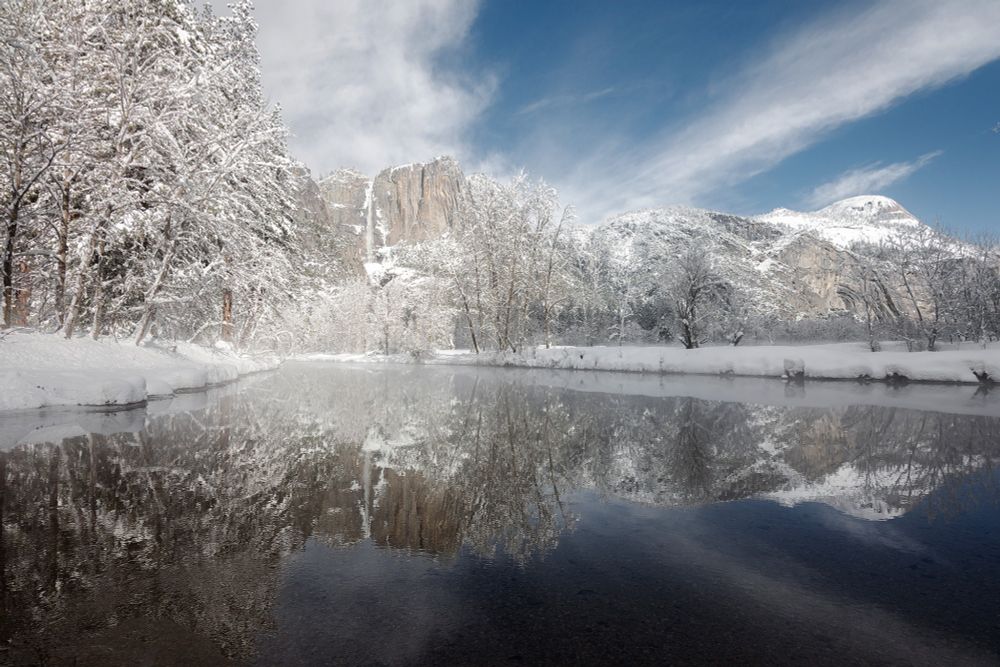 A snowy view of Yosemite Falls reflecting in the Merced River as seen from Swinging Bridge in winter