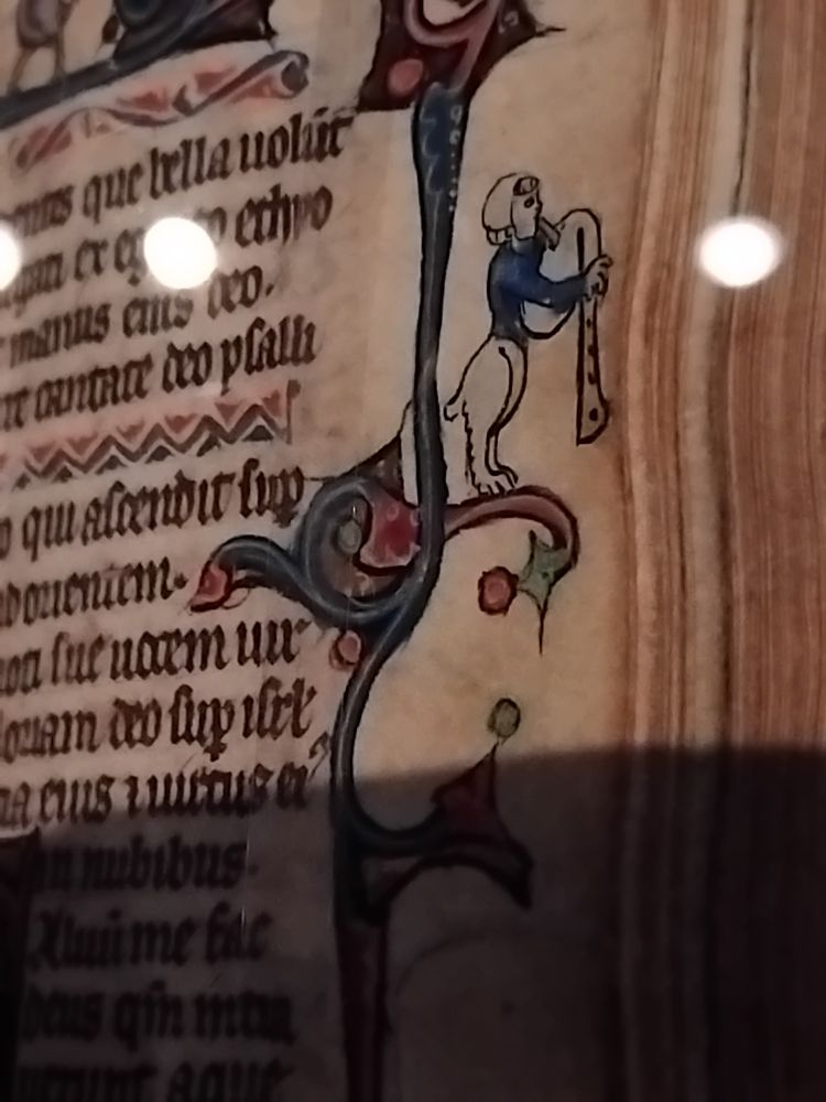 Marge d'un manuscrit. Une créature mi chien mi humain joue d’une sorte de trompe.