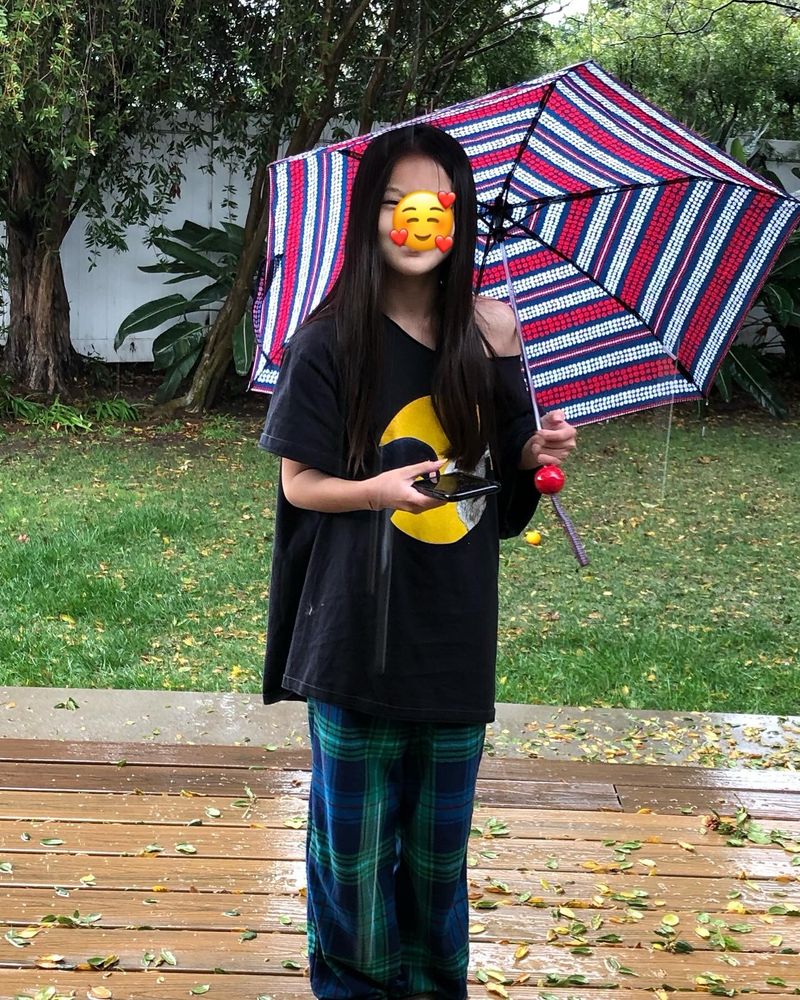 Girl with long dark hair standing in the rain, holding a striped umbrella.