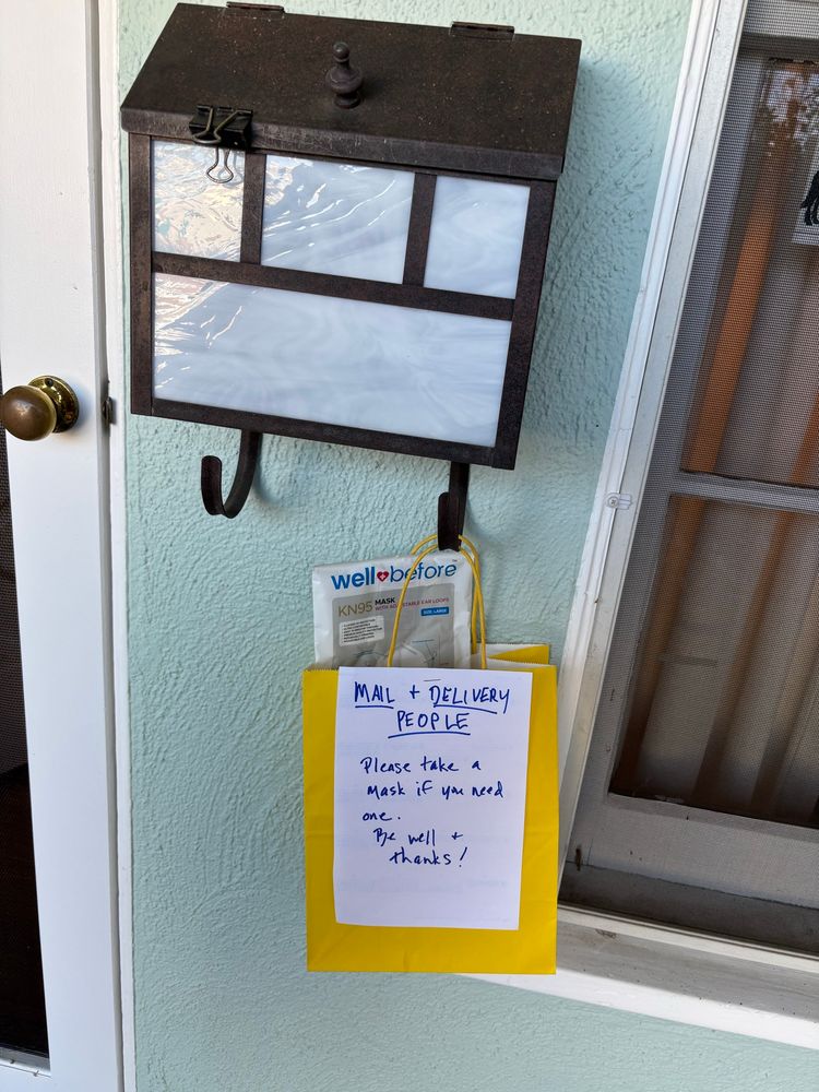A bag of KN95 masks hanging from a mailbox, with a note that tells mail and delivery people to help themselves.