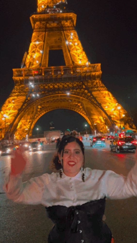 a woman stands in front of an eiffel tower at night