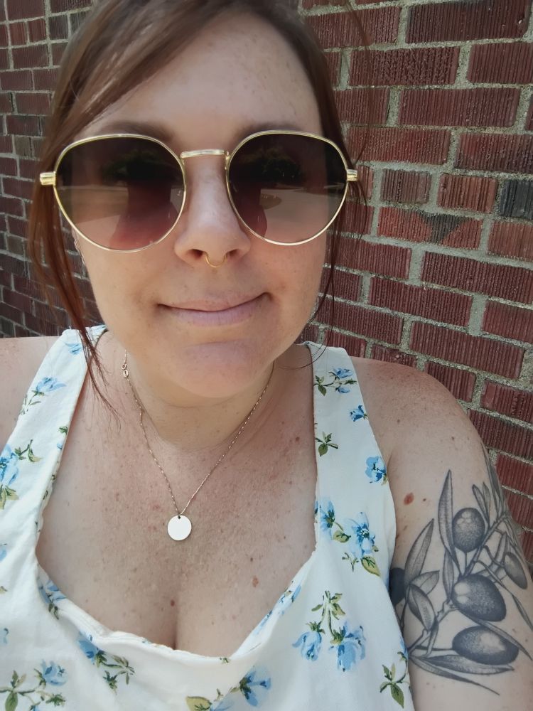 Selfie of me in sunglasses and a floral linen tank top in front of a brick wall