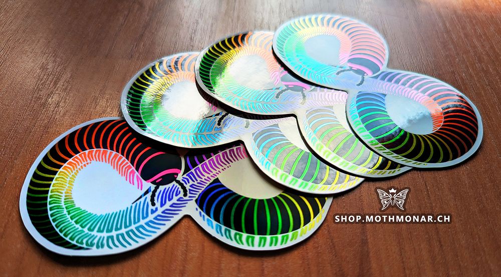 Several infinity symbol shaped stylized millipede stickers with metallic rainbow stripes are fanned out on a wood floor.