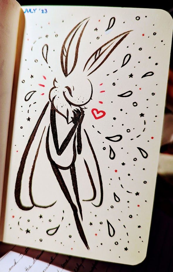 Sketchbook open to a freckled cartoon moth in black ink, smiling with closed eyes and holding their hands over their upper chest. Red dashes and a heart are drawn near their head, with the rest of the space filled by stars, dots, long teardrop shapes, dashed lines, and similar decorative bits.