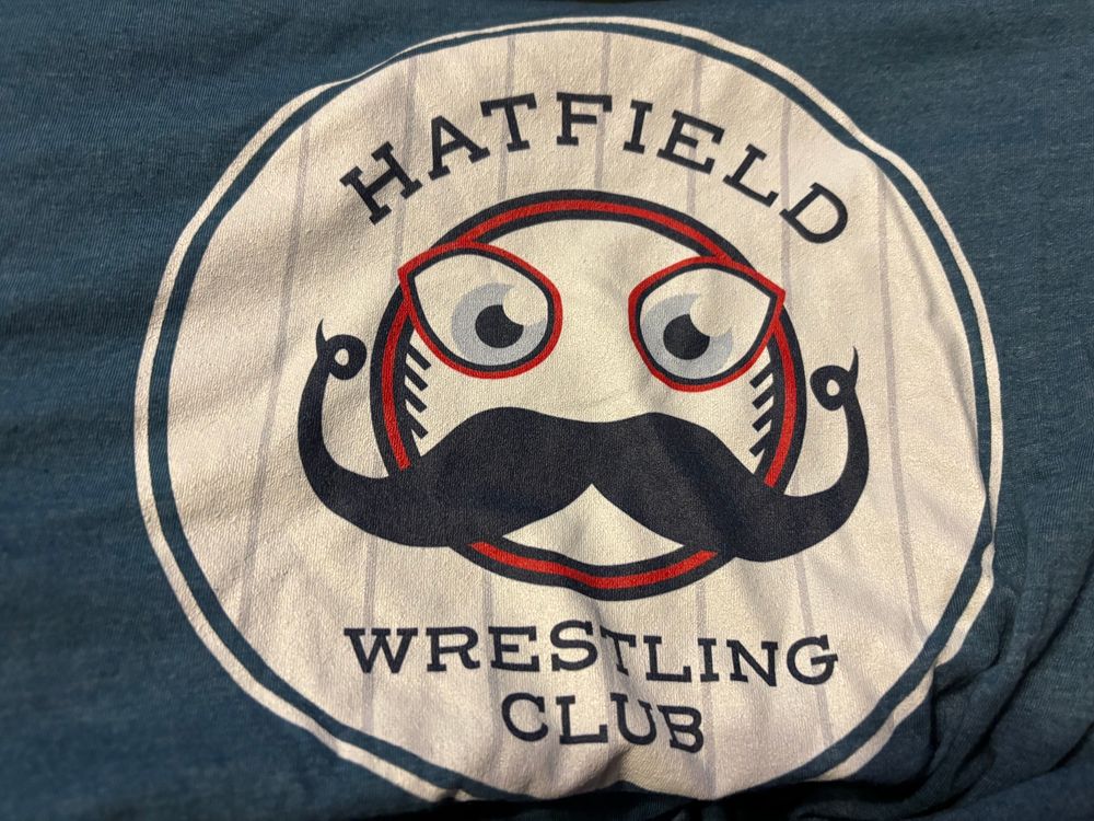 Hatfield Wrestling Club shirt featuring a baseball with eyes and a curly mustache.
