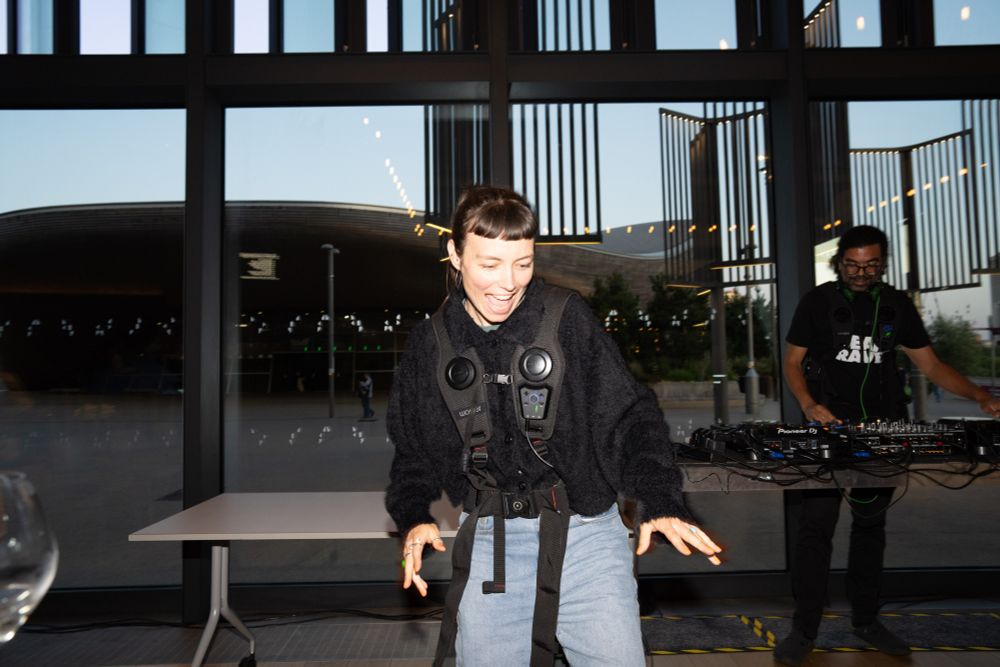 A person wearing a black vibrating vest dances joyfully, smiling widely.