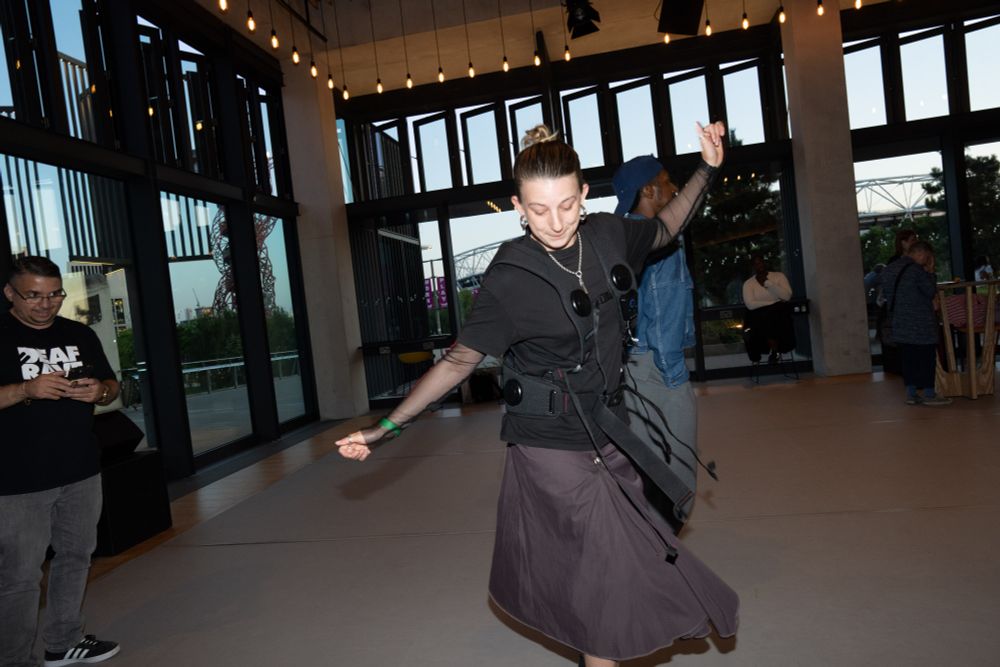 A person wearing a black vibrating vest dances joyfully, smiling widely.