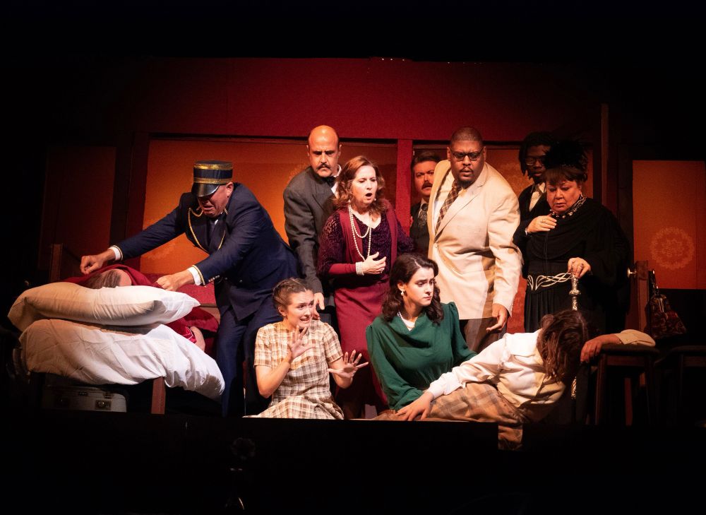 A scene from the stage play A Murder on the Orient Express performed at Starkville Community Theatre. Eleven actors are onstage surrounding a supposed dead body. They are all shocked and/or mid-scream.