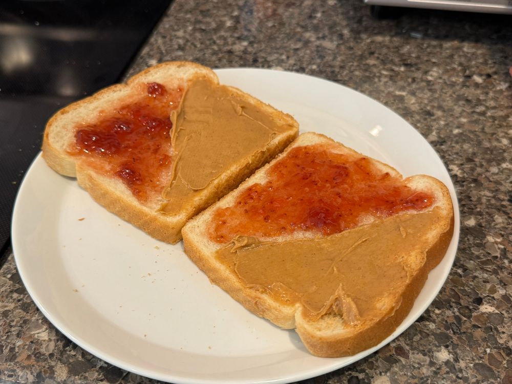 Opened peanut butter and jelly sandwich. Each slice is divided between peanut butter and jelly on the diagonal so that the opposite faces one another once the sandwich is assembled.