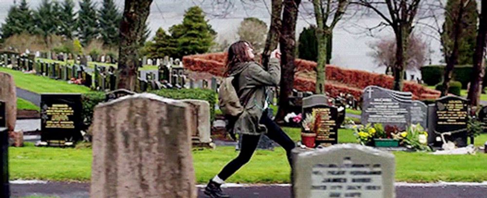 a woman is taking a picture in a cemetery with a gravestone that says " james "