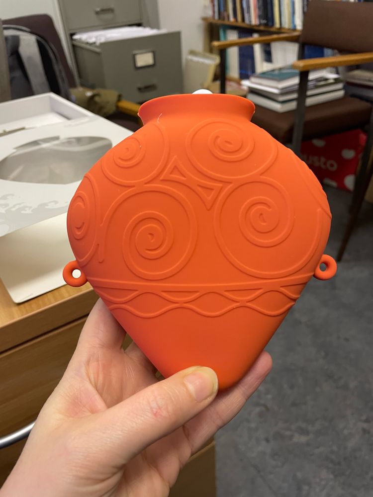 A small hand held water bottle shaped like a ceramic vase, decorated with raised swirls. 